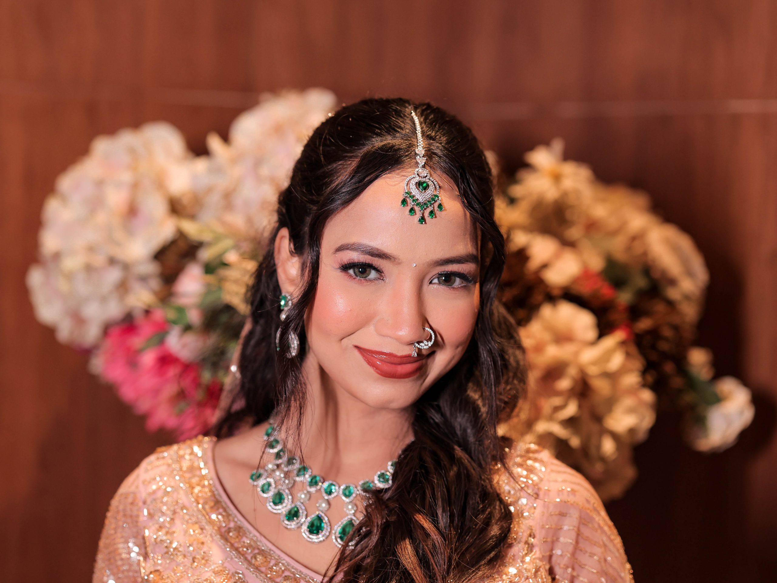 Bride wearing peach bridal outfit with emerald green jewellery and soft glam makeup